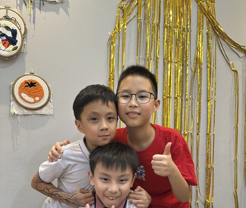 Three boys pose together with thumbs up in front of a gold tinsel backdrop