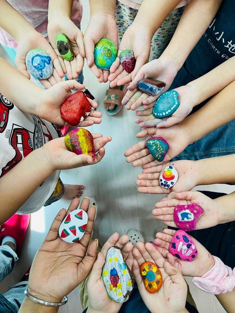 A circle of children's hands, each holding a brightly painted stone